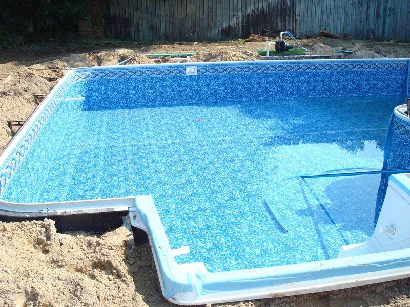 Partially constructed rectangular swimming pool with blue tiled liner and surrounding sand.