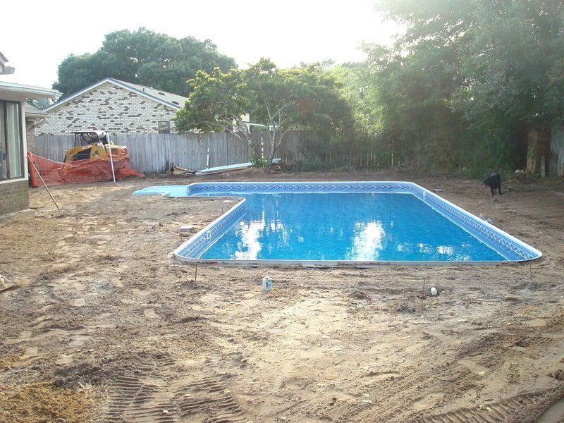 Newly constructed rectangular swimming pool in a dirt backyard; small construction equipment and a dog are visible.