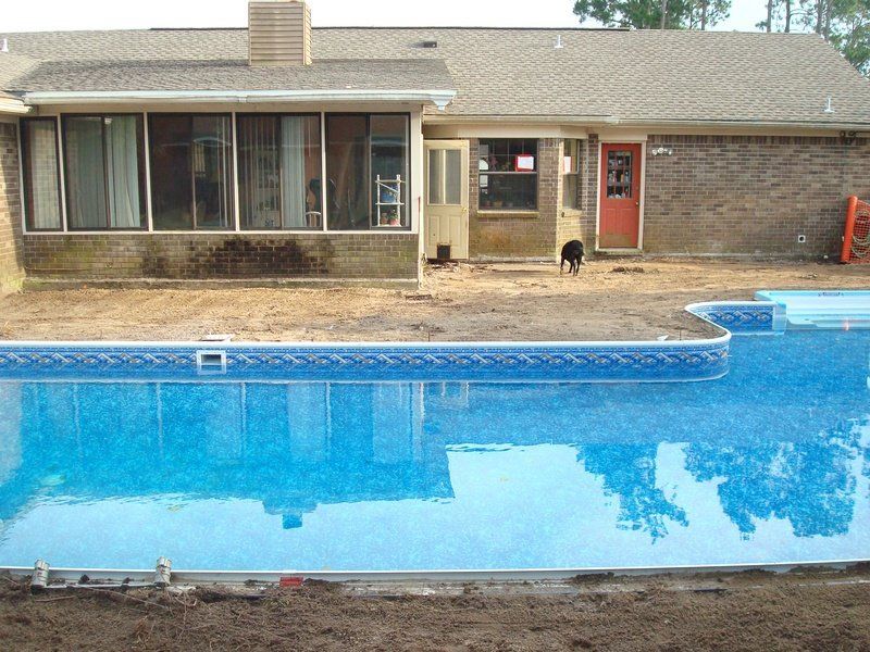 Backyard with pool, house with screened porch and red door. Pool water reflects trees.