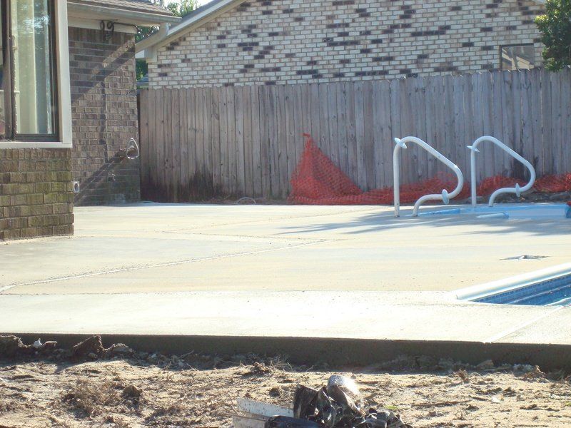 Concrete pool deck with white handrails and wooden fence in the background.