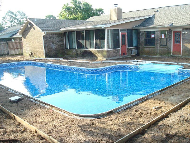 Swimming pool under construction in a backyard, blue liner, surrounding dirt, and a house.