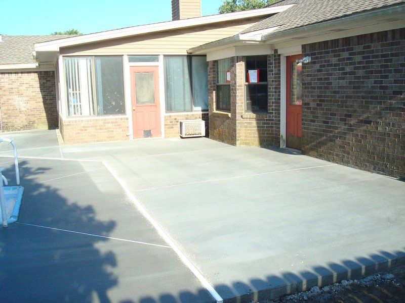 Exterior view of a brick building with a concrete patio; a sunroom is on the left.
