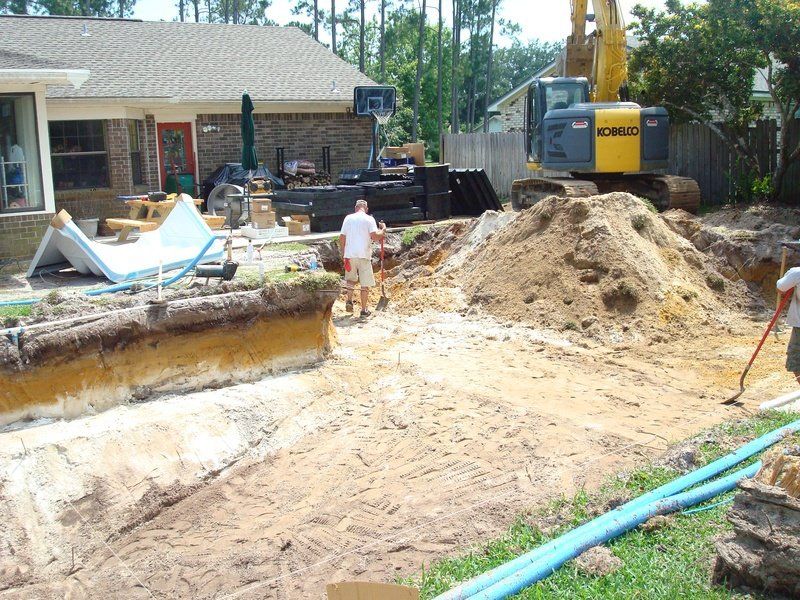 Backyard pool construction site with excavator, workers, and excavated soil.