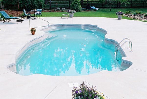 A kidney-shaped swimming pool filled with blue water, surrounded by a concrete patio.