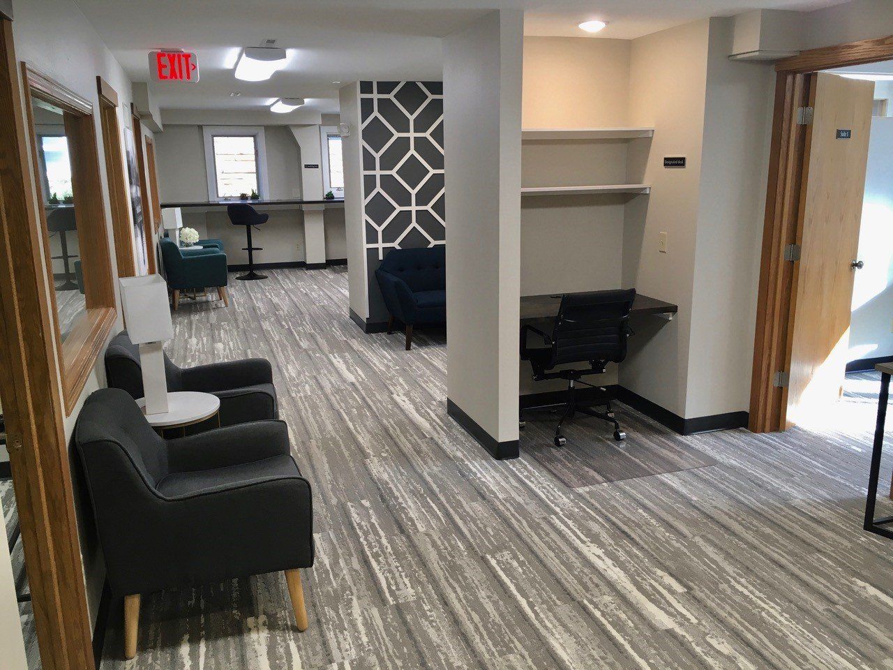 Lounge area with seating, desk, and decorative wall panel. Grey and white patterned flooring.
