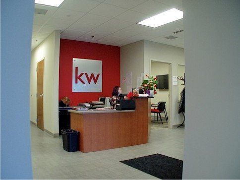 Reception area of Keller Williams real estate office with a person at the desk. Red and white logo on red wall.
