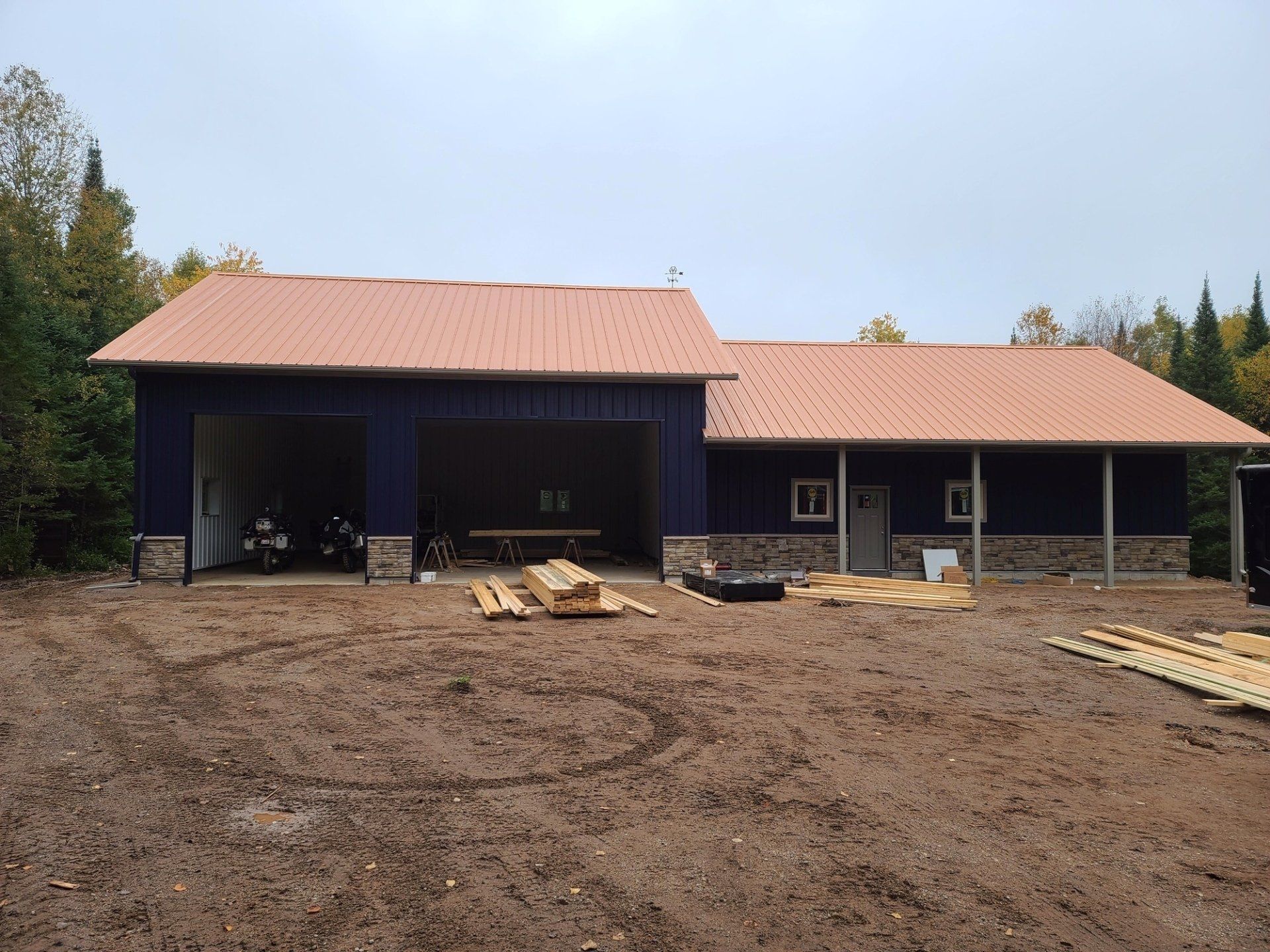 Blue building with orange roof, open garage, wood piles. Muddy yard.