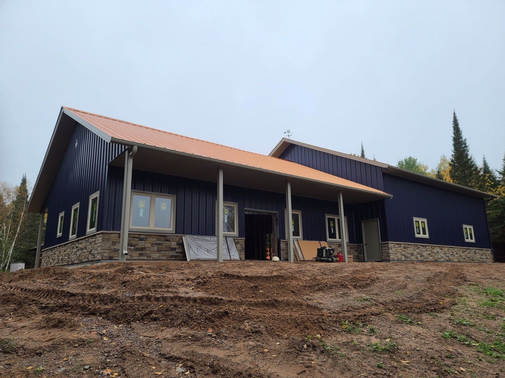Blue-sided building under construction with a stone base and orange roof. Cloudy, outdoor setting.