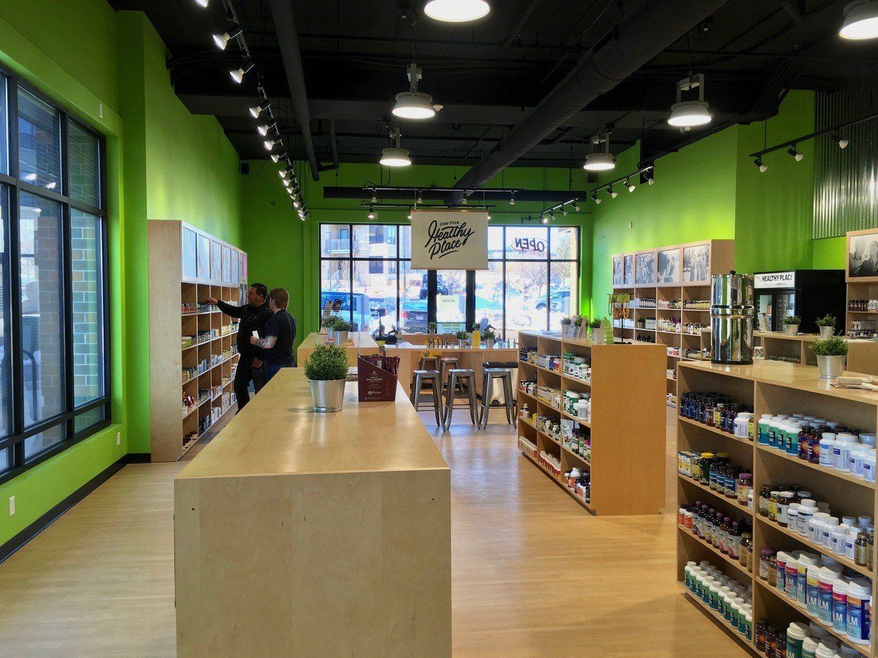 Interior of a health store with bright green walls, wooden shelves, and customer browsing.