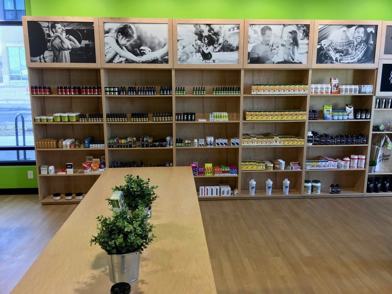Interior of a store, shelves stocked with products, overhead photos, wooden table with plant.