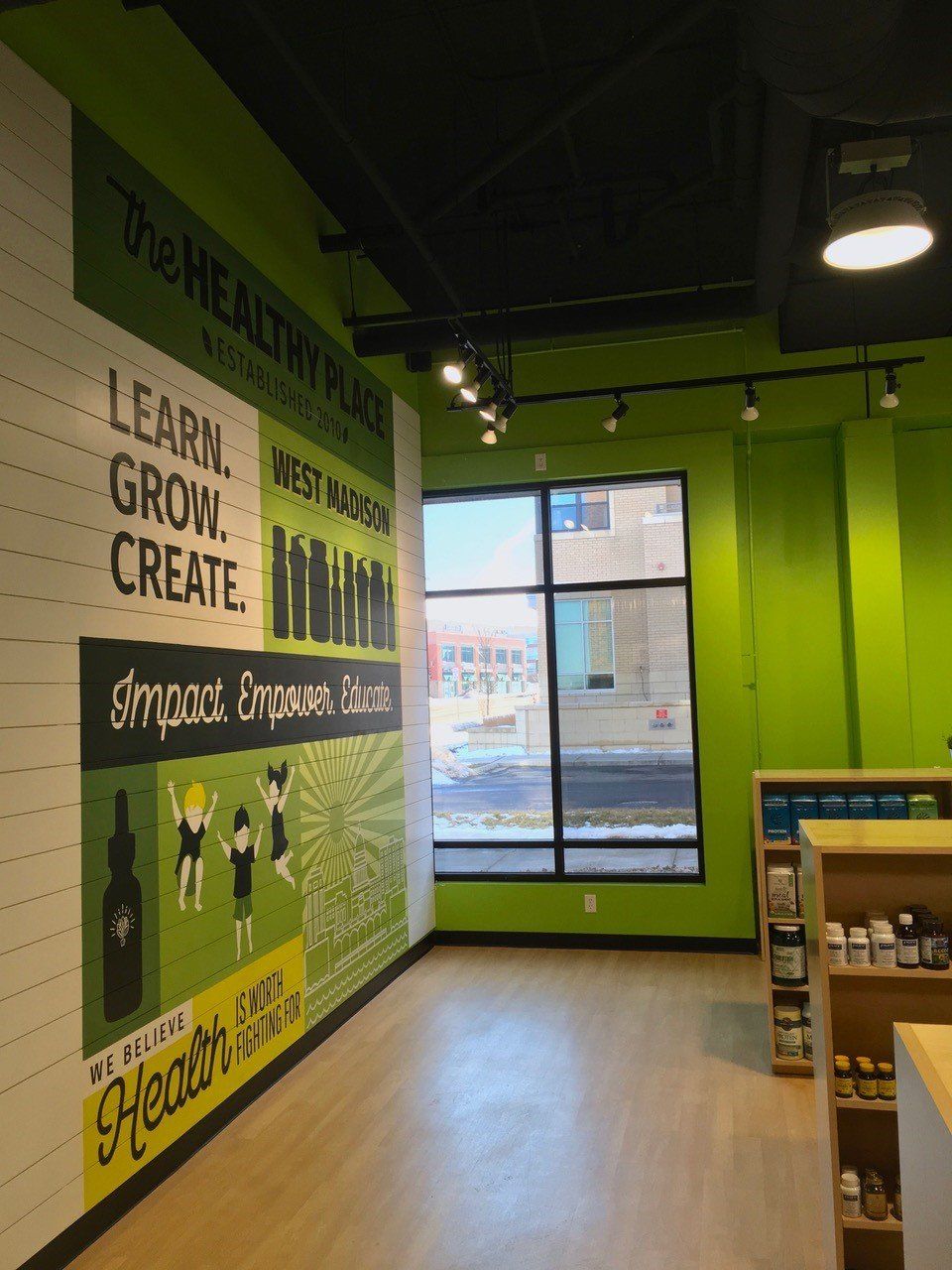 Interior of The Healthy Place retail store with green and black accents. Mural with text on wall.