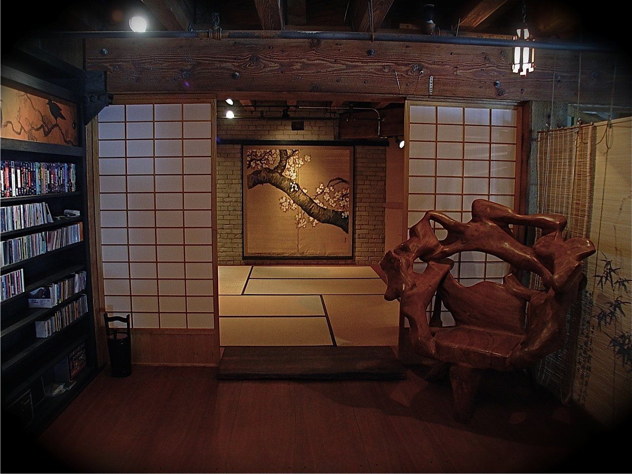 Japanese-style interior with wooden beams, sliding doors, a sculpted chair, and a bookcase.