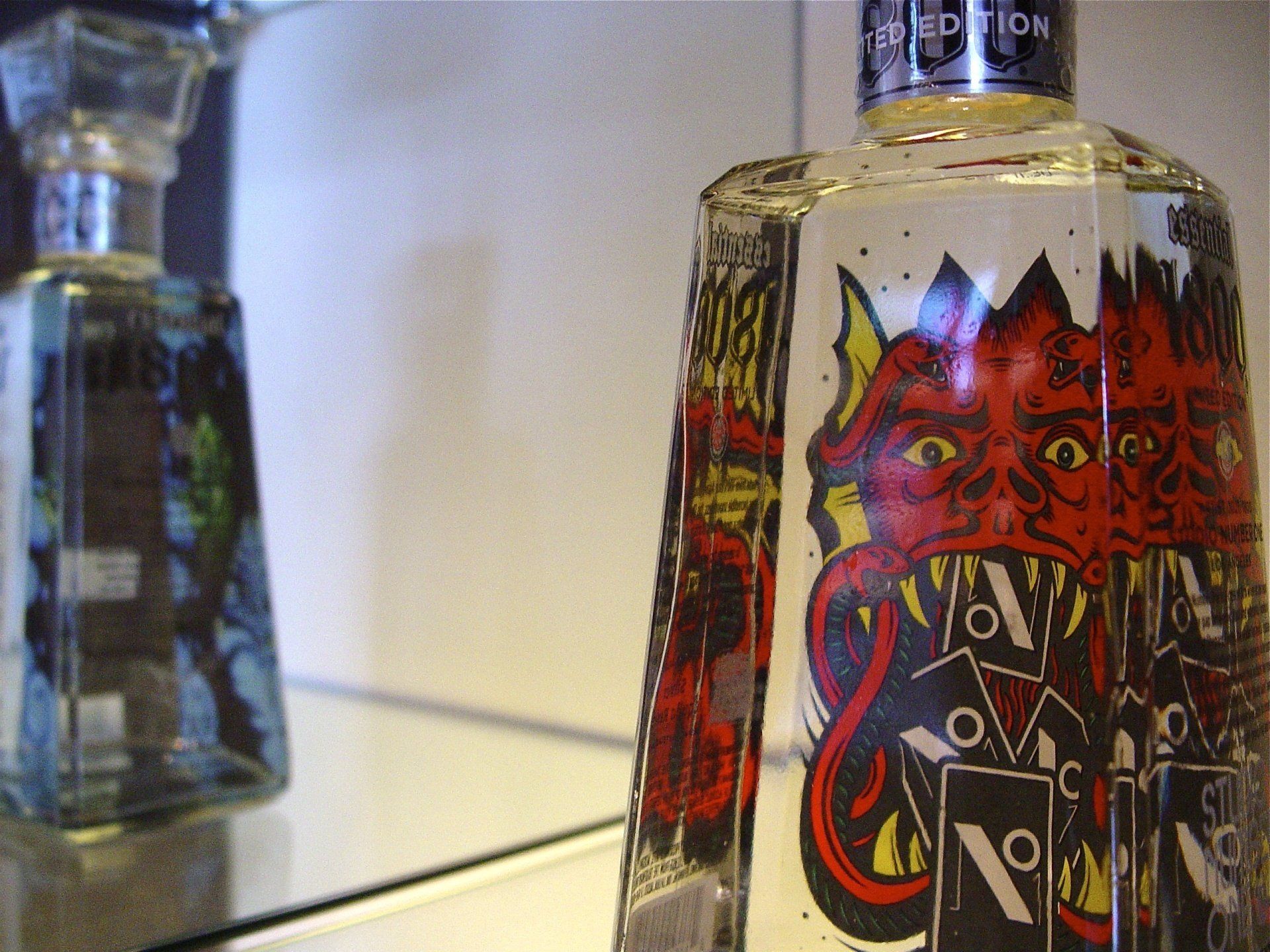 Two bottles of liquor, one with a red devil graphic, on a reflective surface.