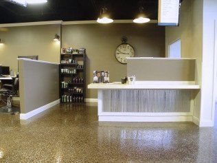 Reception area of a hair salon. Gray walls, shiny concrete floor, modern decor, clock, and product display.