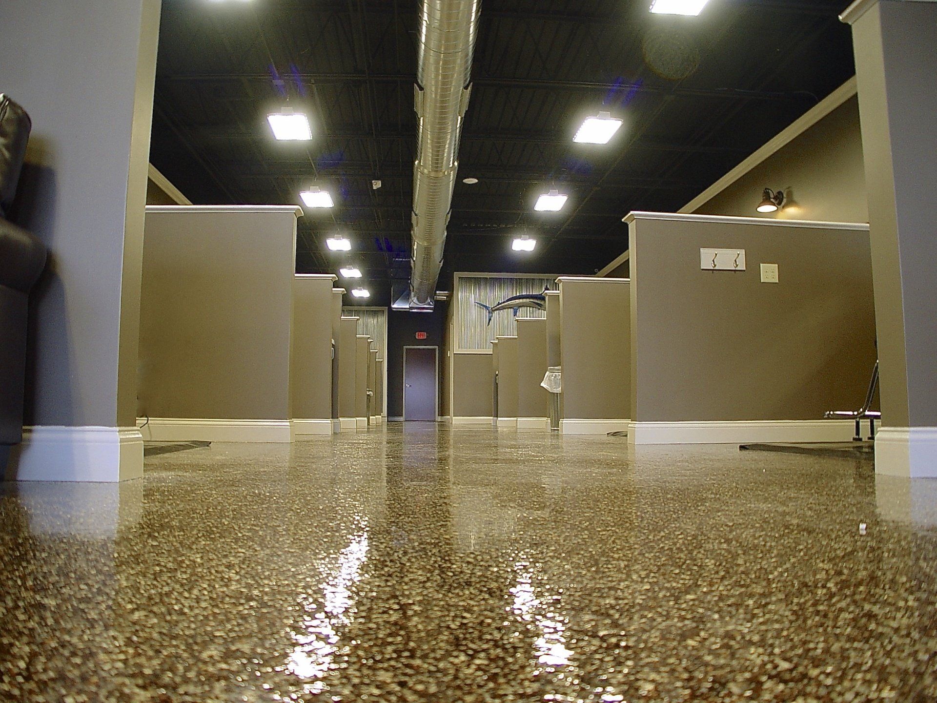 Bathroom with brown pebble-covered floor, stalls, and ceiling lights, reflecting light.