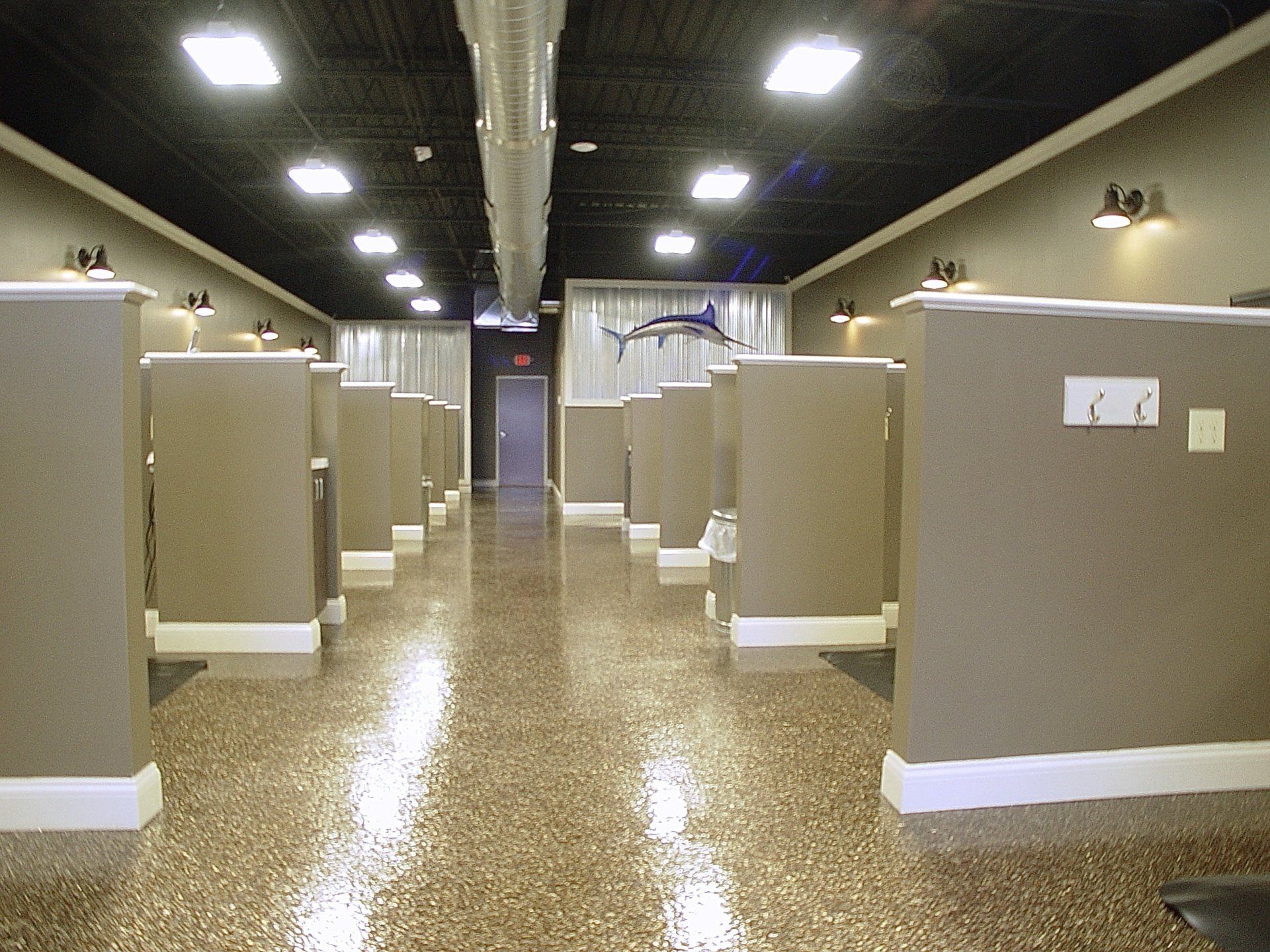Empty interior with cubicles, shiny speckled floor, dark ceiling, and a hallway leading to a door.