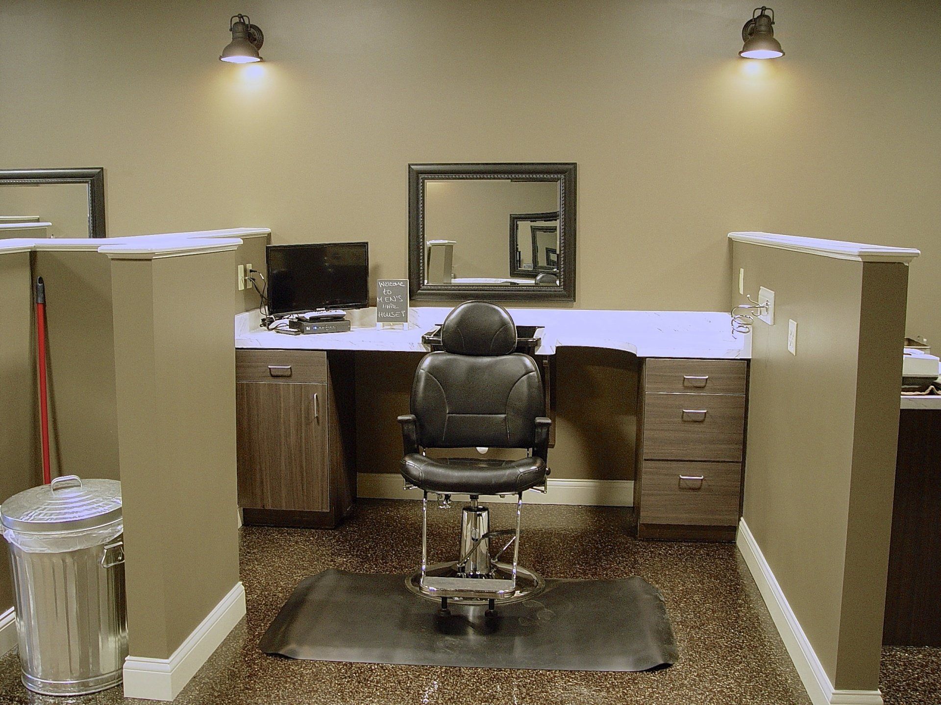 Hair salon station with chair, mirror, and cabinetry. Beige walls, speckled floor.