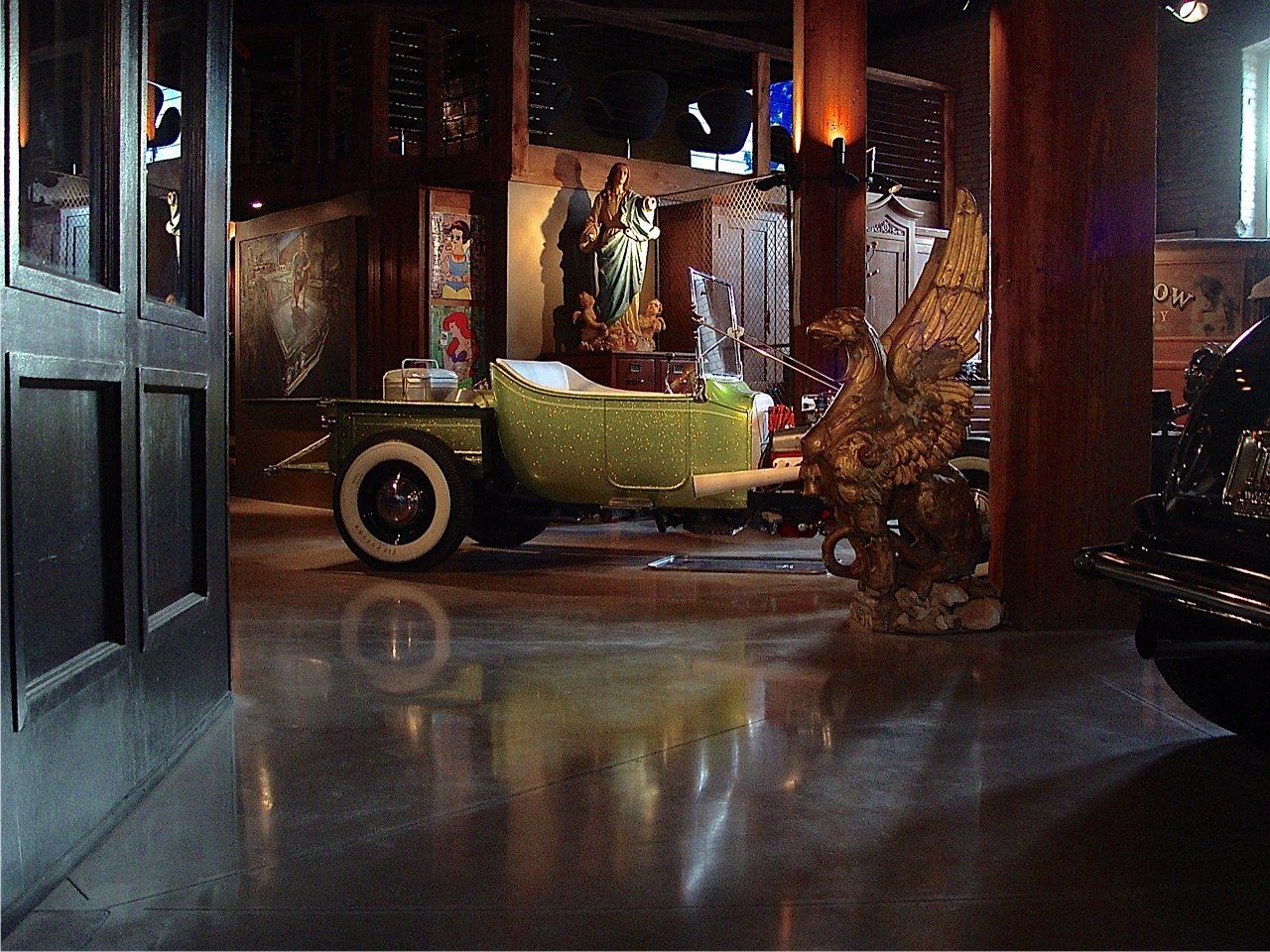 Green vintage car inside a dimly lit, ornate interior. Reflective floor, statue visible in background.