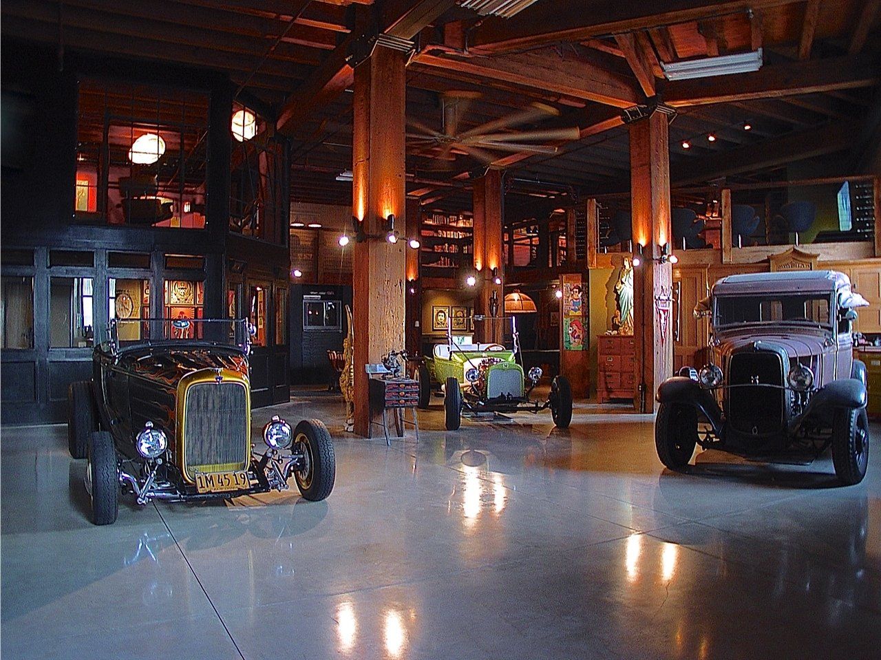 A large hall with vintage cars on display, wooden pillars, and ambient lighting.