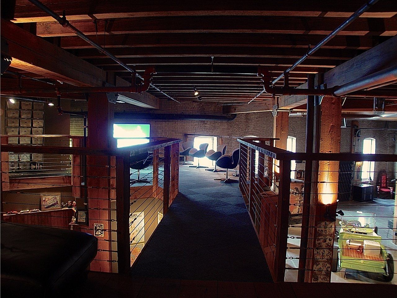 Interior of a rustic building with exposed brick, wooden beams, and a mezzanine overlooking the main floor.