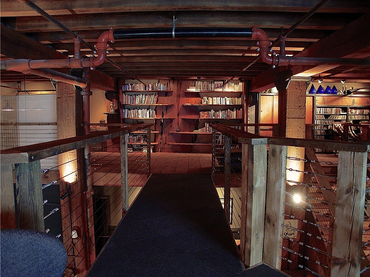 Library interior with bookshelves, a walkway, and exposed pipes.