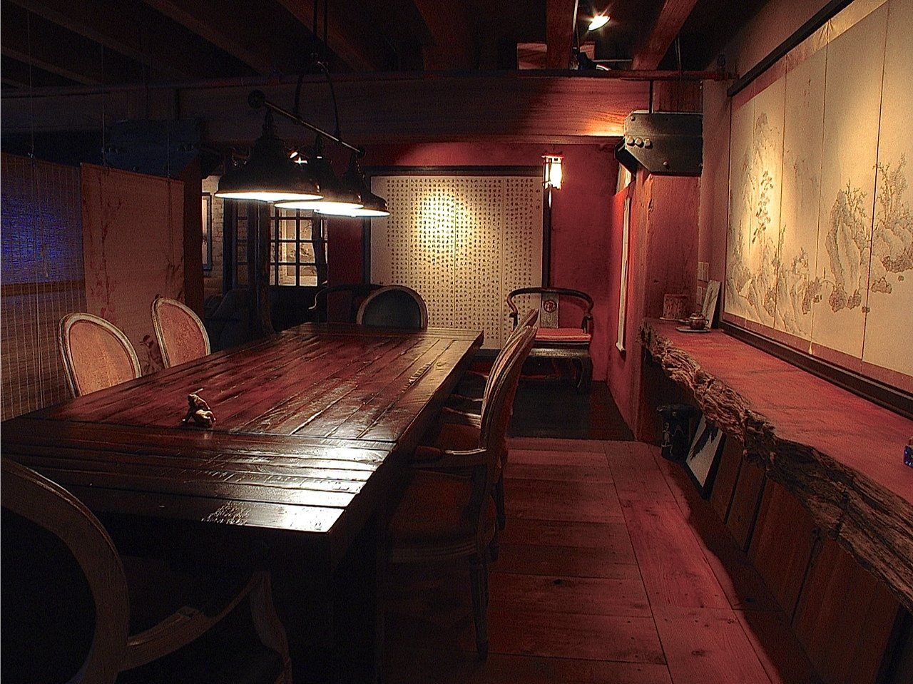 Dimly lit dining room with long wooden table, chairs, and ornate wall art.