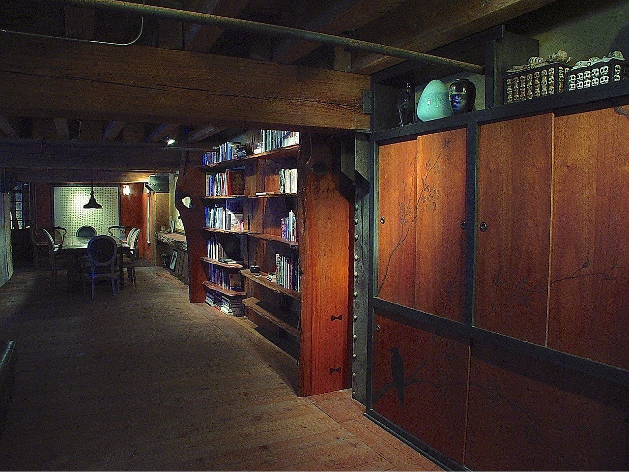 A dimly lit library or study with built-in wooden bookshelves and cabinets.