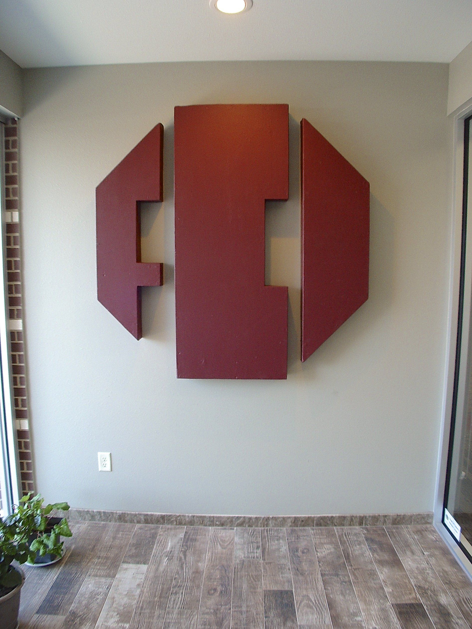Red geometric wall sculpture on a light beige wall; interior setting.