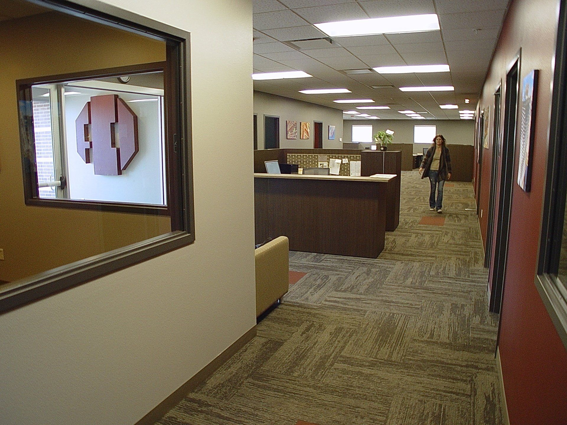 Office hallway with a person walking, reception desk, and decorative wall art.