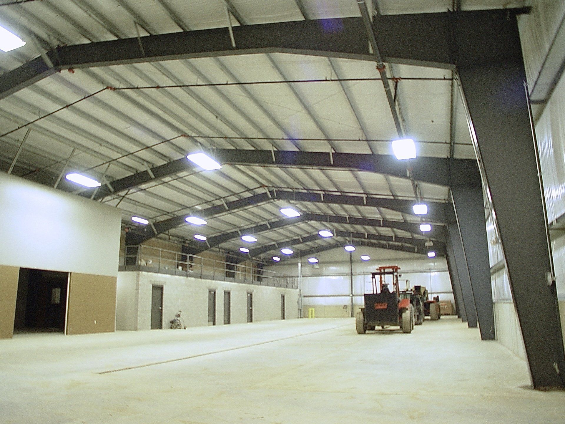 Interior of a large metal building with a tractor; overhead lighting and support beams are visible.