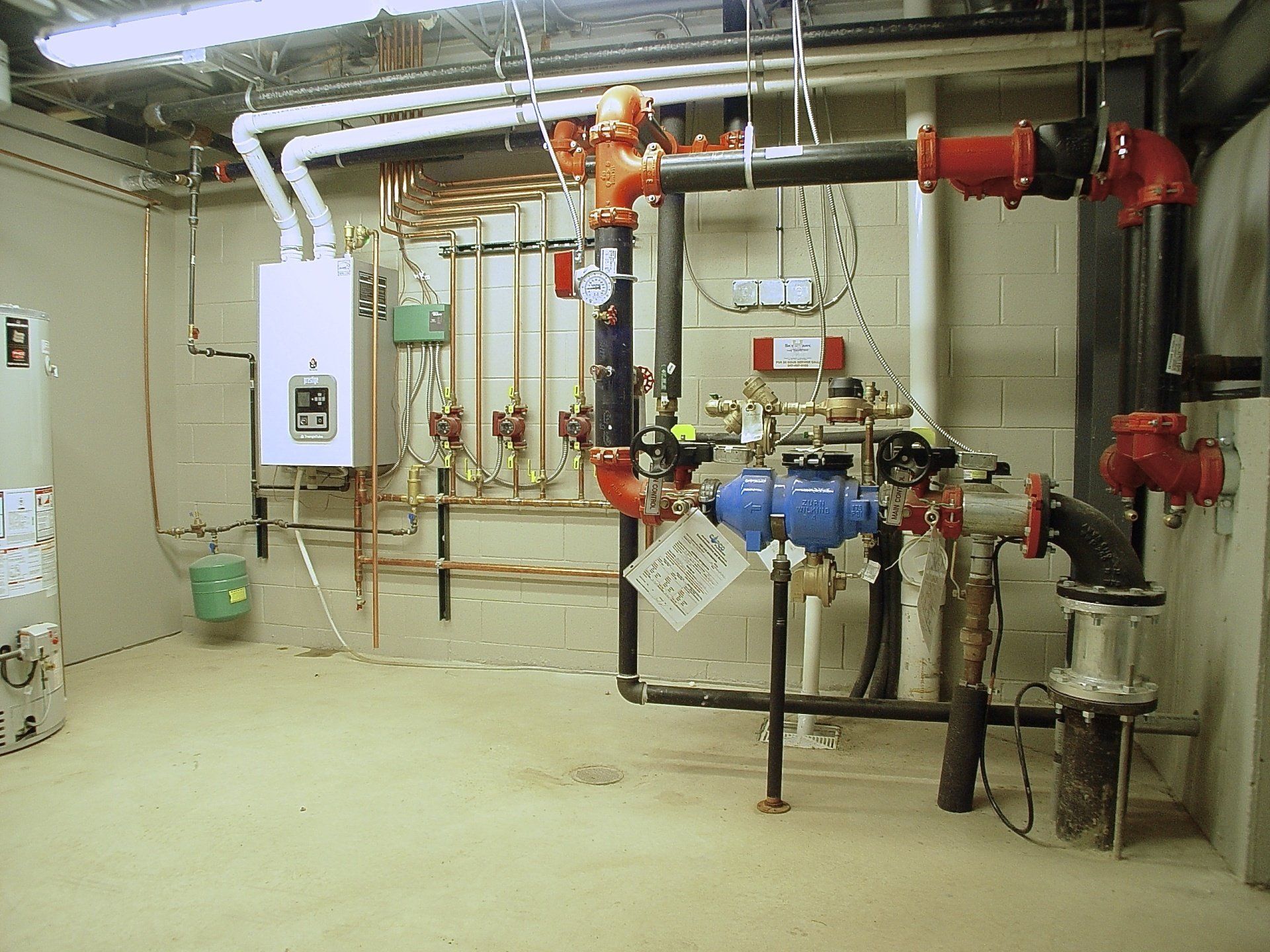 Boiler room with pipes, valves, and a water heater, featuring copper and black pipes with red valves.