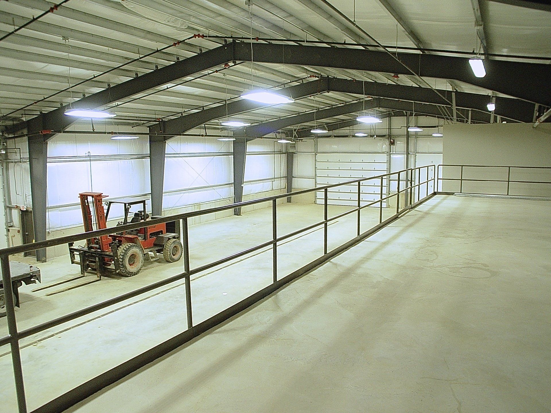 Inside a large warehouse with a tractor, a metal railing, and overhead lighting.