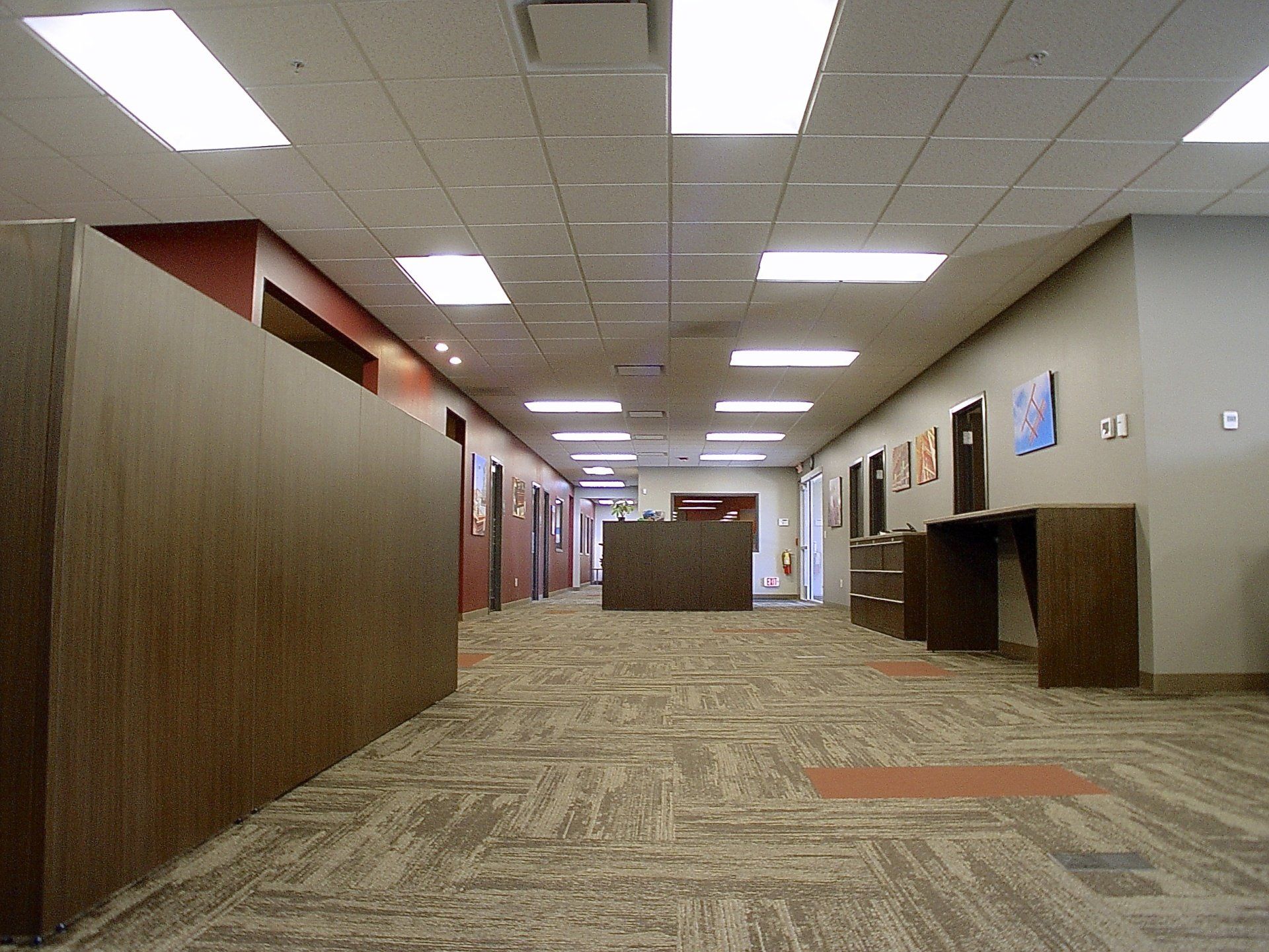 Hallway with brown paneled walls and carpet, leading to more doors and a reception desk.