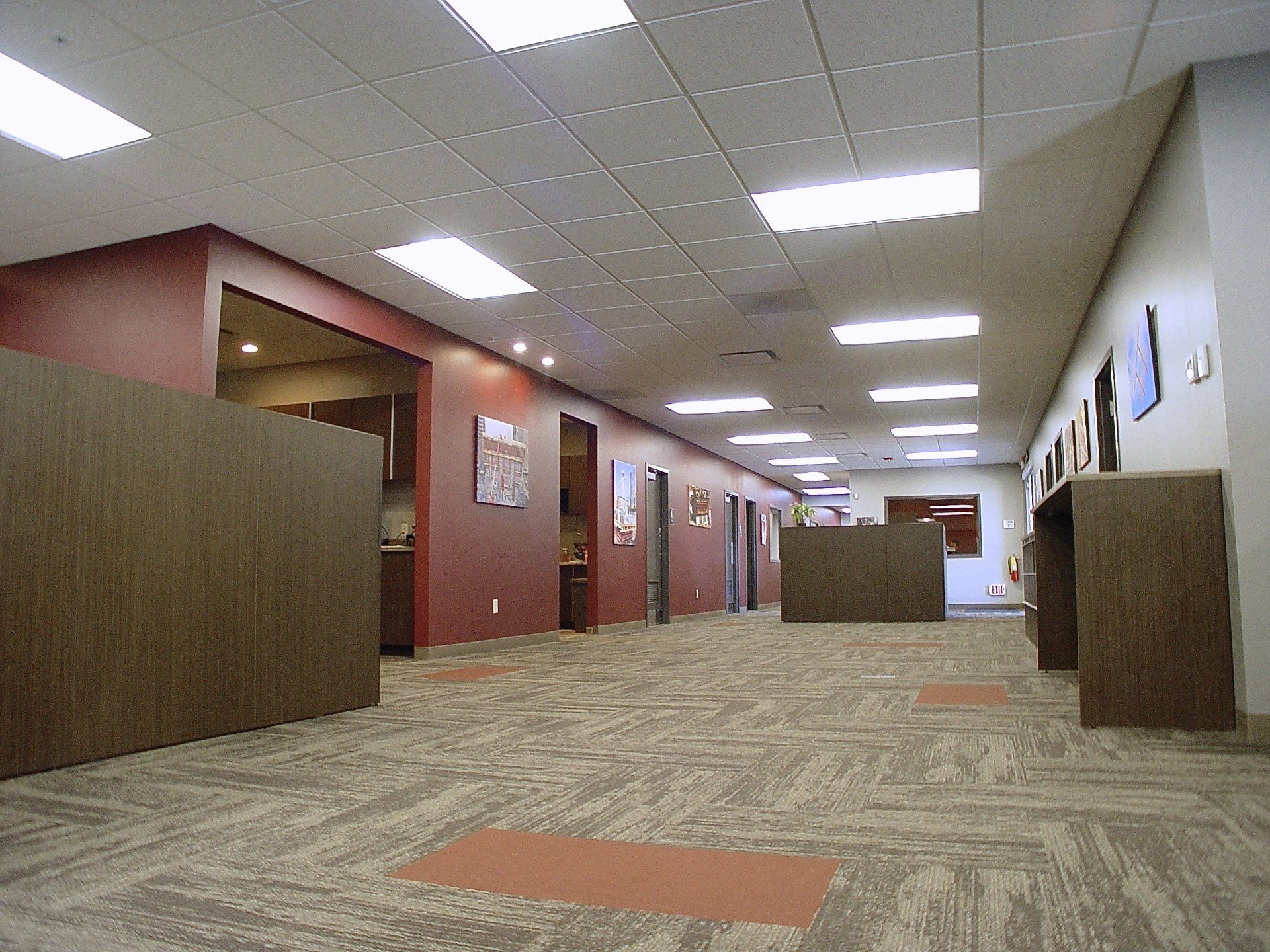 Office hallway with brown and red walls, tan carpet, and recessed lighting.