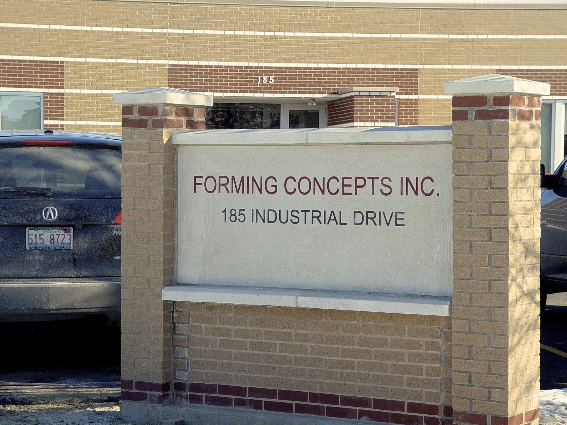 Sign for Forming Concepts Inc., 185 Industrial Drive, with a brick and concrete structure, with a car visible.