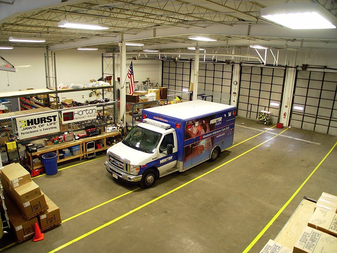 Ambulance inside a large warehouse, marked lanes on floor, shelving with supplies.
