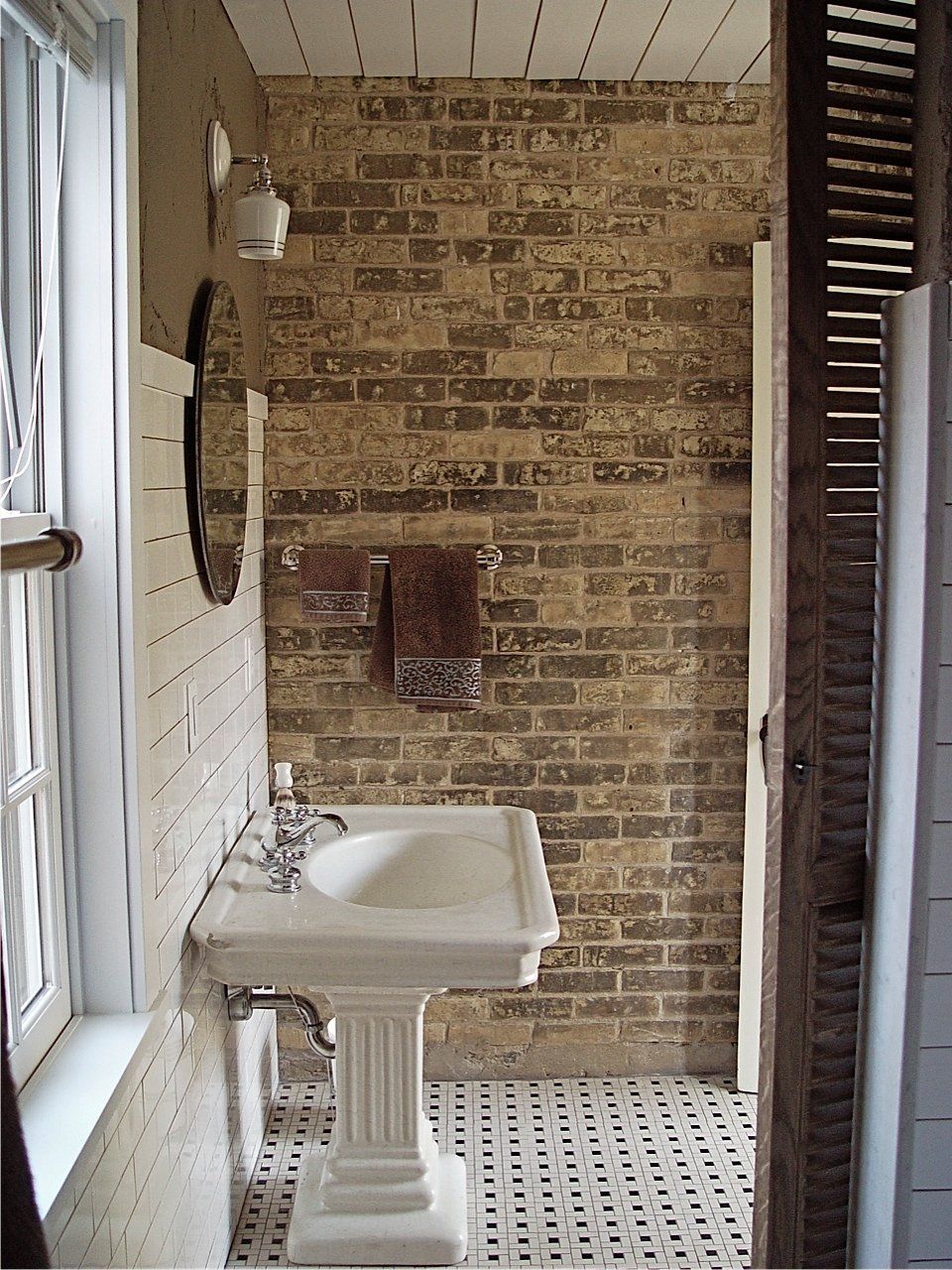 Bathroom with brick wall, pedestal sink, and checkered tile floor.