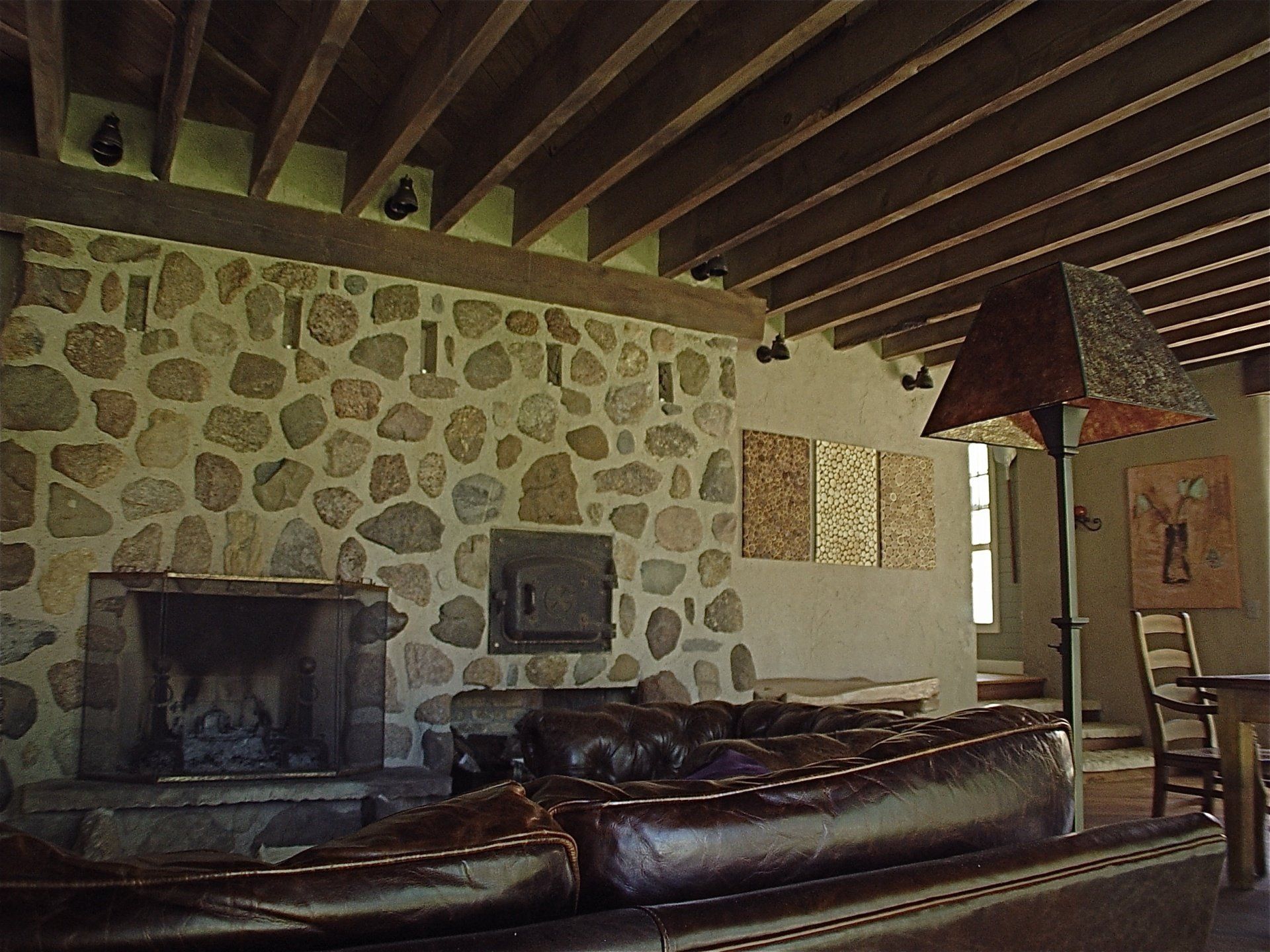 Living room with stone fireplace, brown leather couch, and wood-beam ceiling.