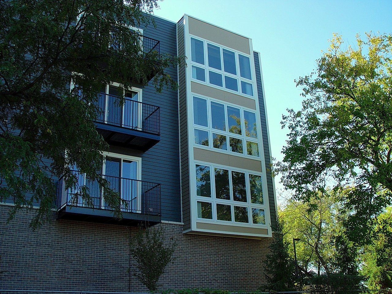 Modern building with balconies and tall windows, exterior view. Blue-gray and tan facade.