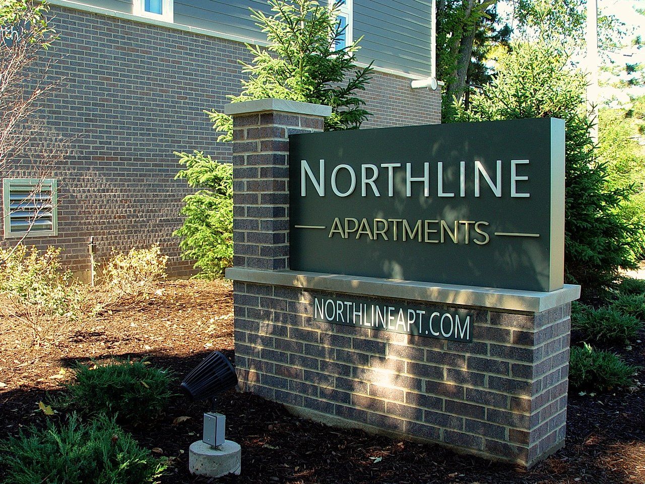 Northline Apartments sign: Brick base with metal sign, website address, and adjacent building.