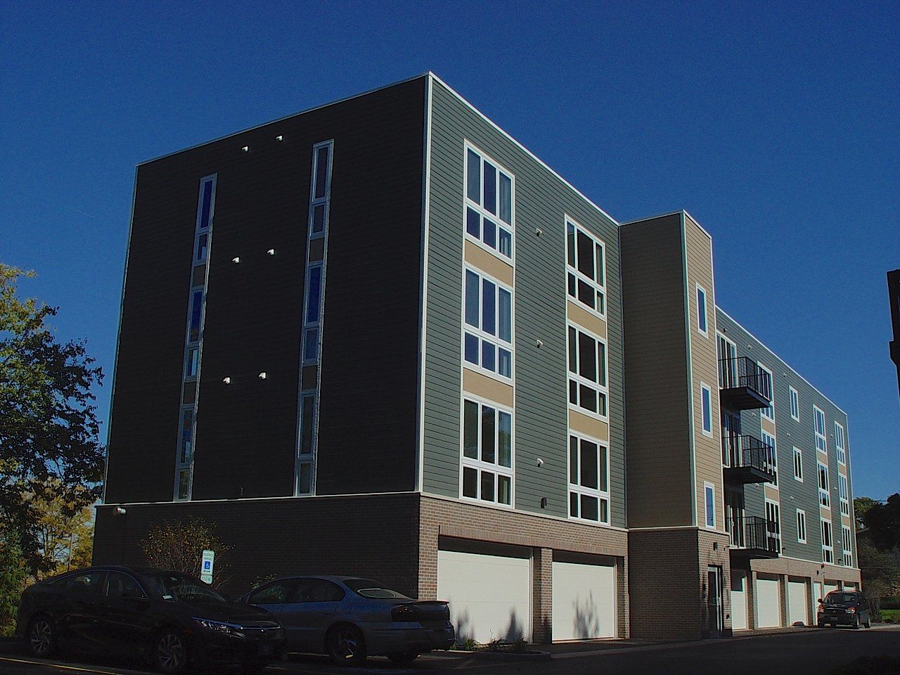 Modern multi-story apartment building with dark green siding and garage parking.