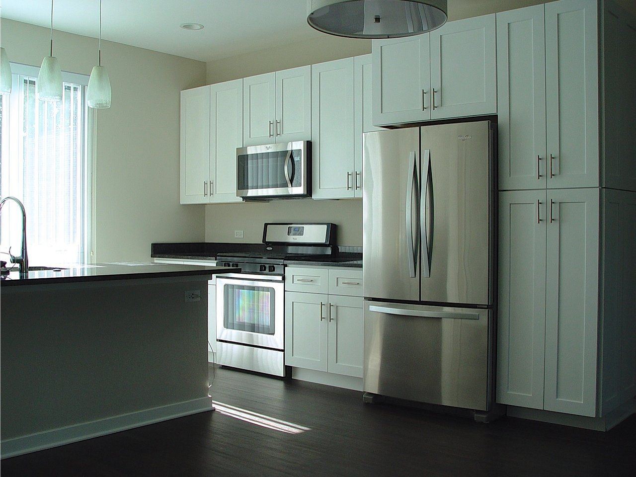 Modern kitchen with white cabinets, stainless steel appliances, dark countertop, and dark wood floor.