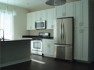 Modern kitchen with white cabinets, stainless steel appliances, dark countertop, and dark wood floor.