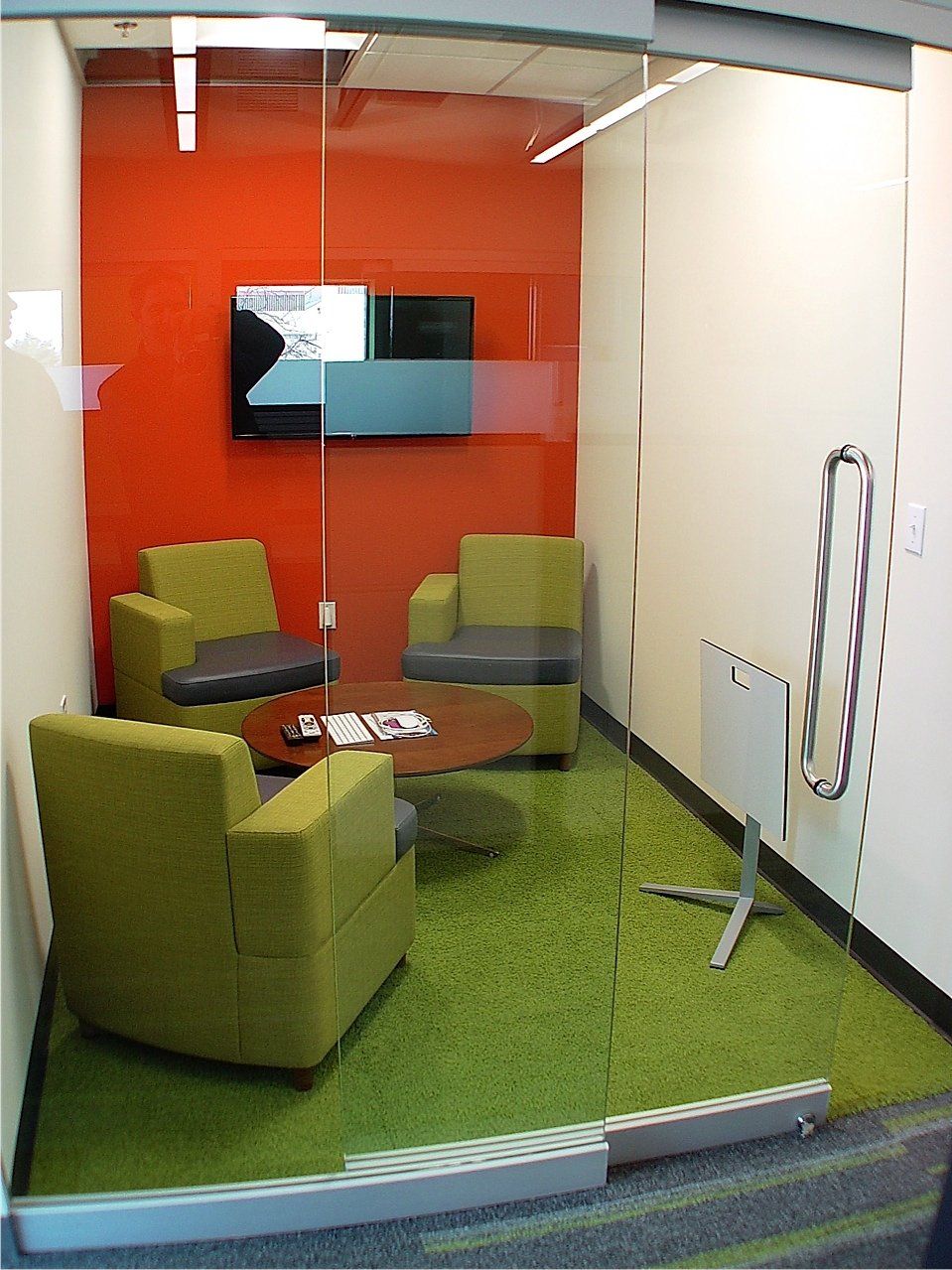 Small office with green carpet, orange and white walls, green chairs, and glass door.