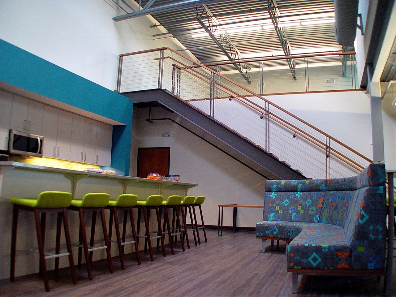 Modern office interior with a staircase, bar seating, and a patterned sofa.