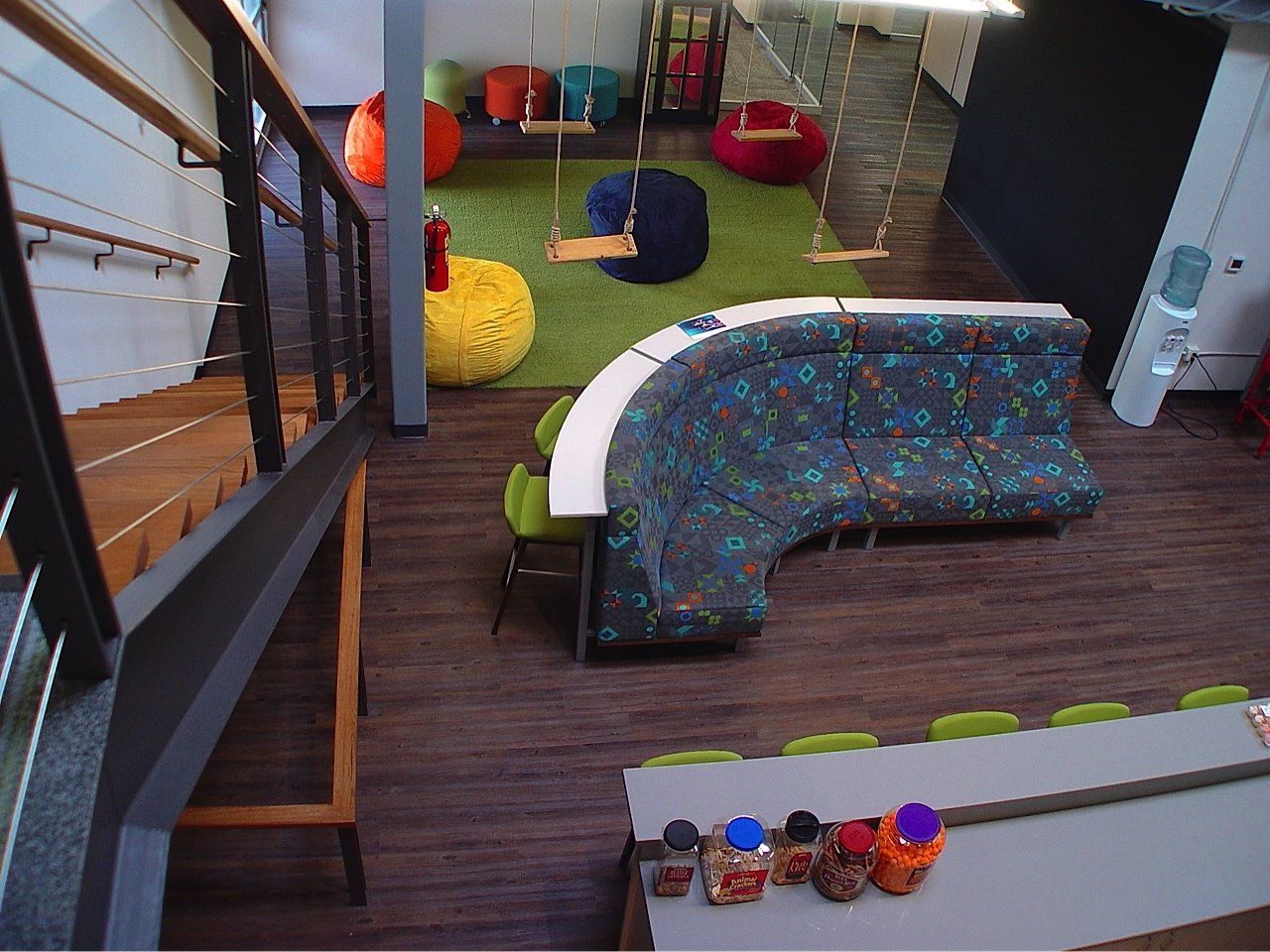 Office lounge with curved blue sofa, swings, stairs, and colorful beanbags.