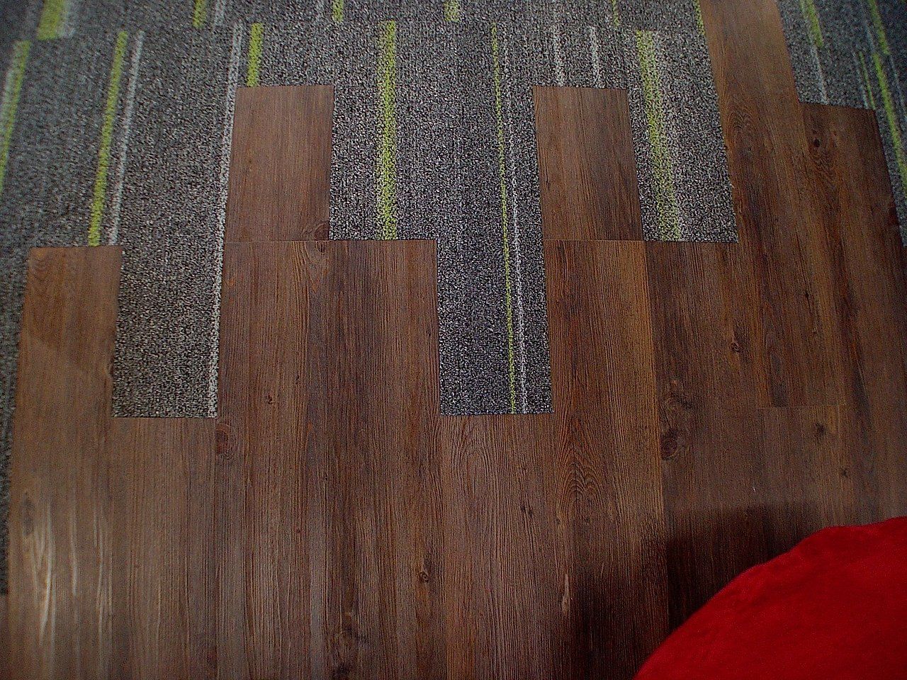Wood-look planks partially installed over a textured carpet, red object in corner.