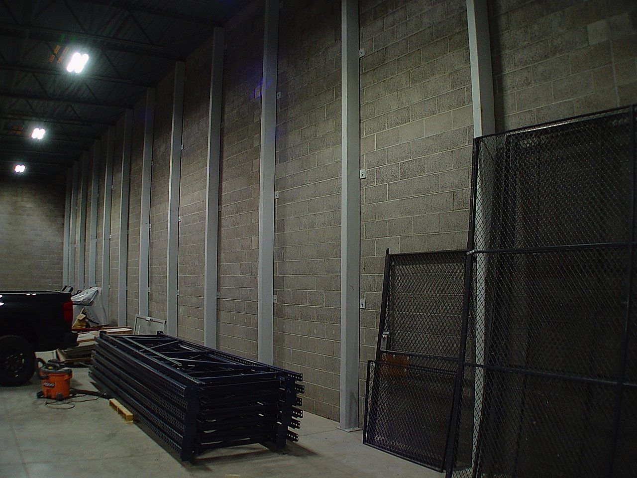 Interior of a large room with metal framing on a wall. Stacks of black metal fencing are in the foreground.