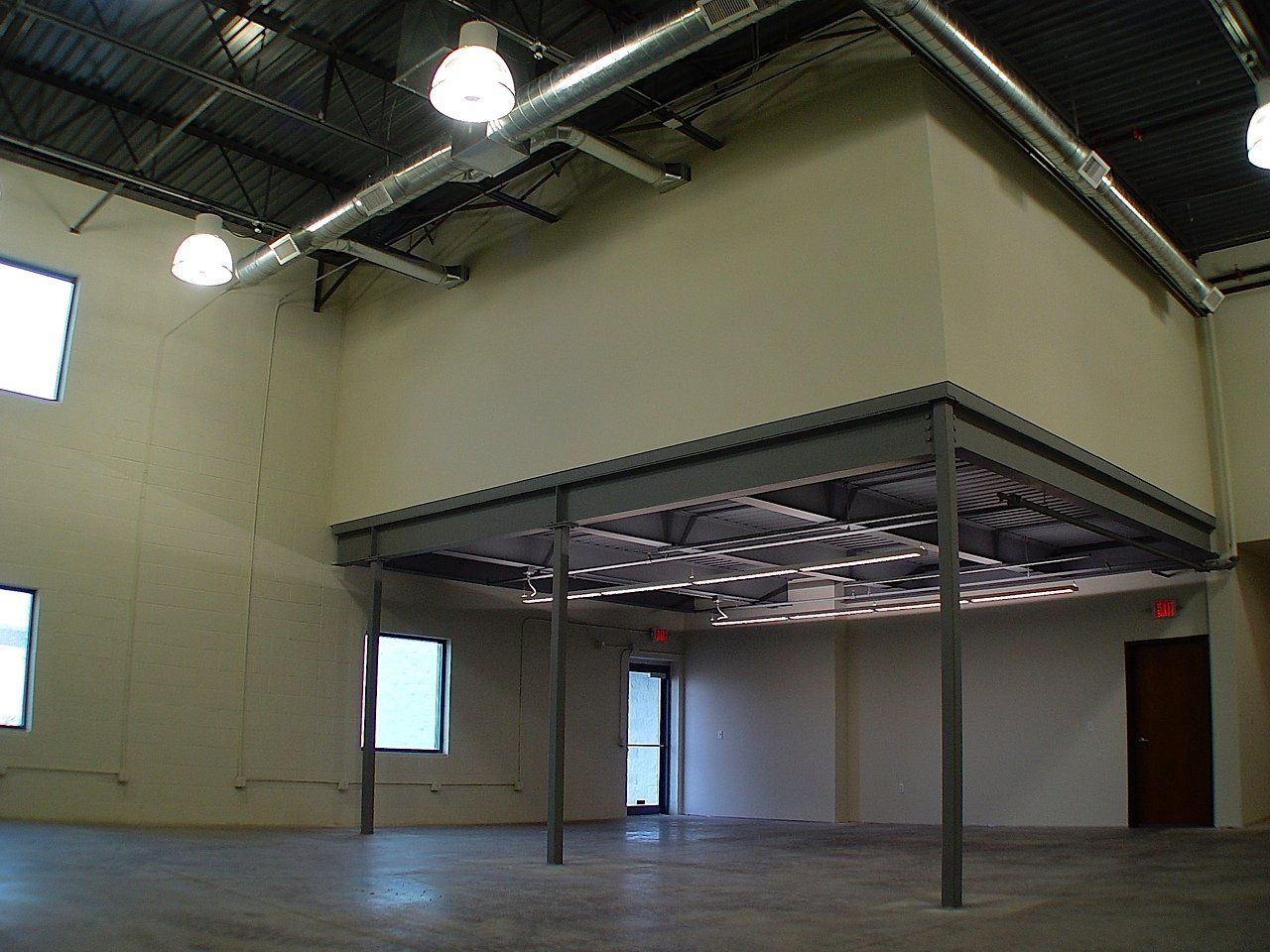 Interior view of a building with a metal mezzanine, windows, and exposed ceiling.