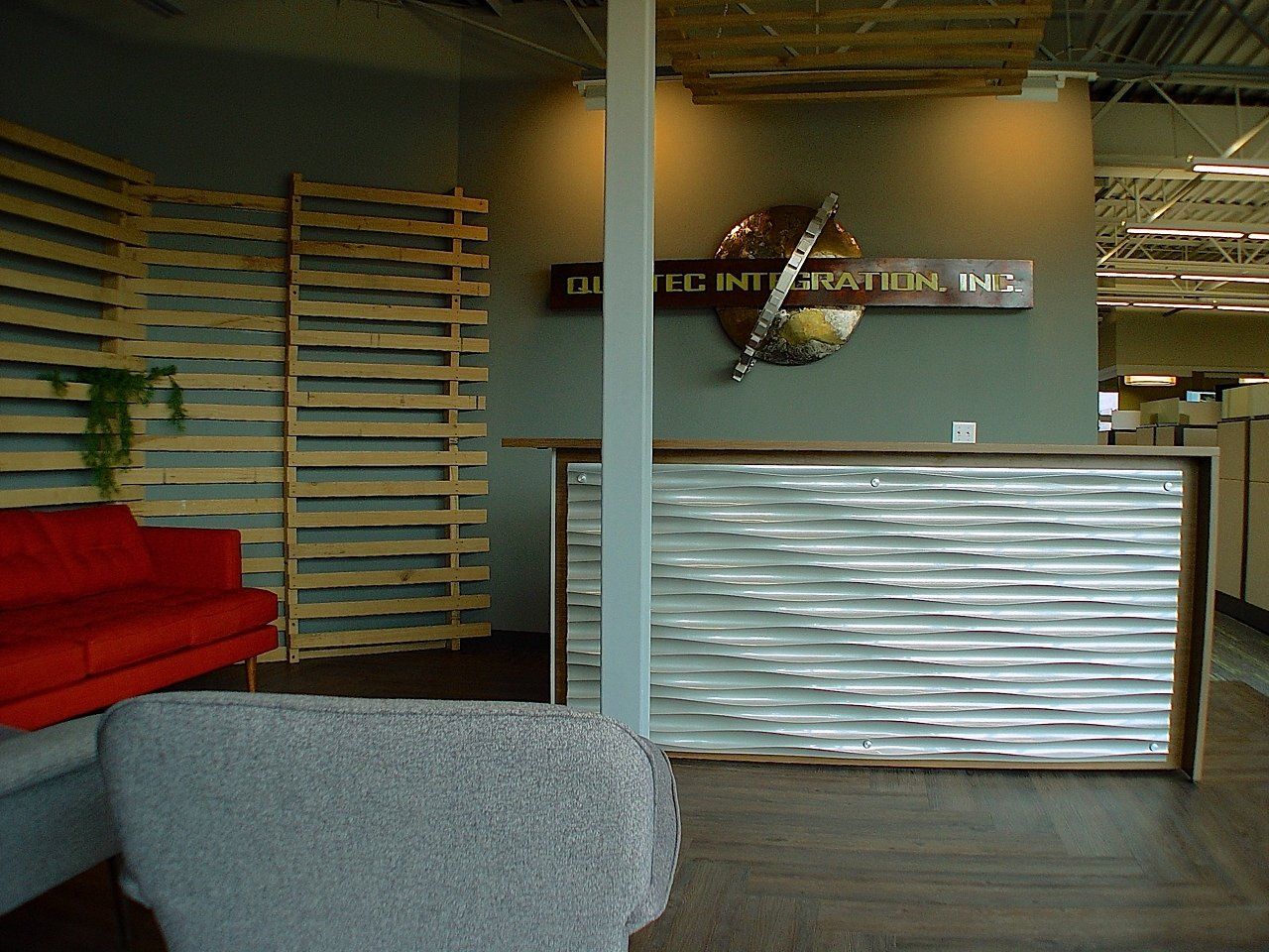 Office lobby with red couch, pallet wall, corrugated metal reception desk, company logo.